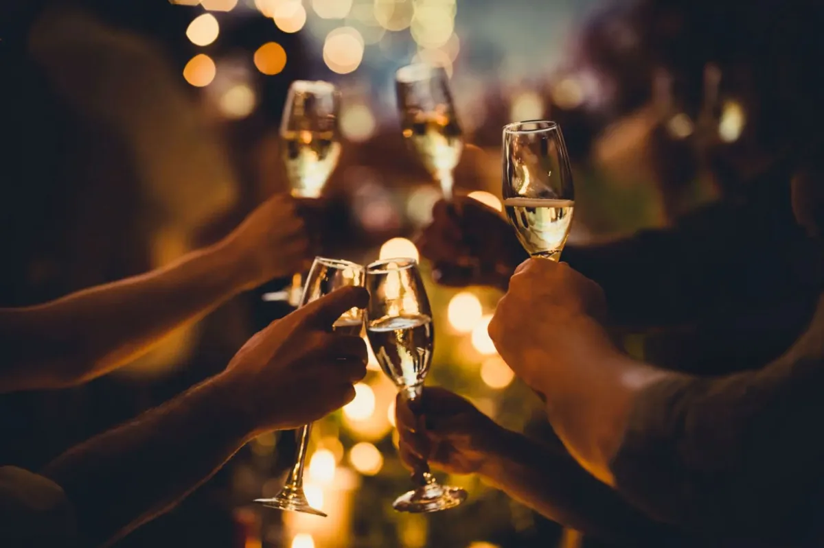Verres de champagne levés pour trinquer, sous des lumières de fête.